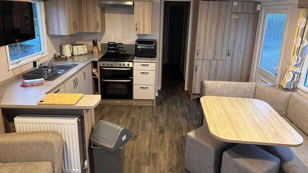 A compact kitchen with a stove, oven, and sink, a dining area with a table and chairs, and a trash bin. - 3br-sleeps6-parking-pool-nearbeach&skegness (Skegness)