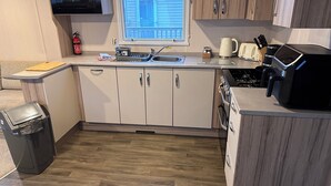 A compact kitchen with a window, wooden cabinets, a microwave, a stove, and a trash bin. - 3br-sleeps6-parking-pool-nearbeach&skegness (Skegness)