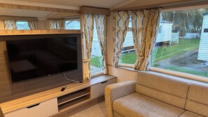 A compact living space with a flat-screen TV, wooden furniture, and a sofa. - 3br-sleeps6-parking-pool-nearbeach&skegness (Skegness)