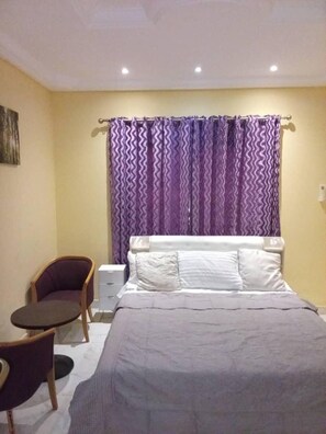 Relax in a cozy space with a neatly made bed, a comfortable chair, and a bedside table.