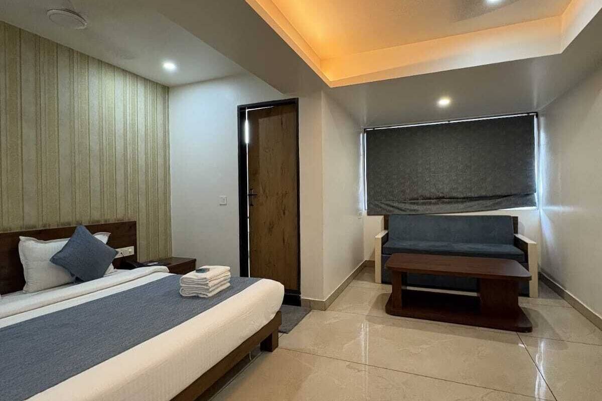 Una habitación de hotel moderna con una cama grande, un banco, un ventilador de techo y una ventana con vistas.