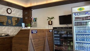 Un espace d’accueil comprenant un comptoir de réception en bois, une horloge, une plante, un réfrigérateur rempli de boissons et un panneau indiquant les heures d’enregistrement.