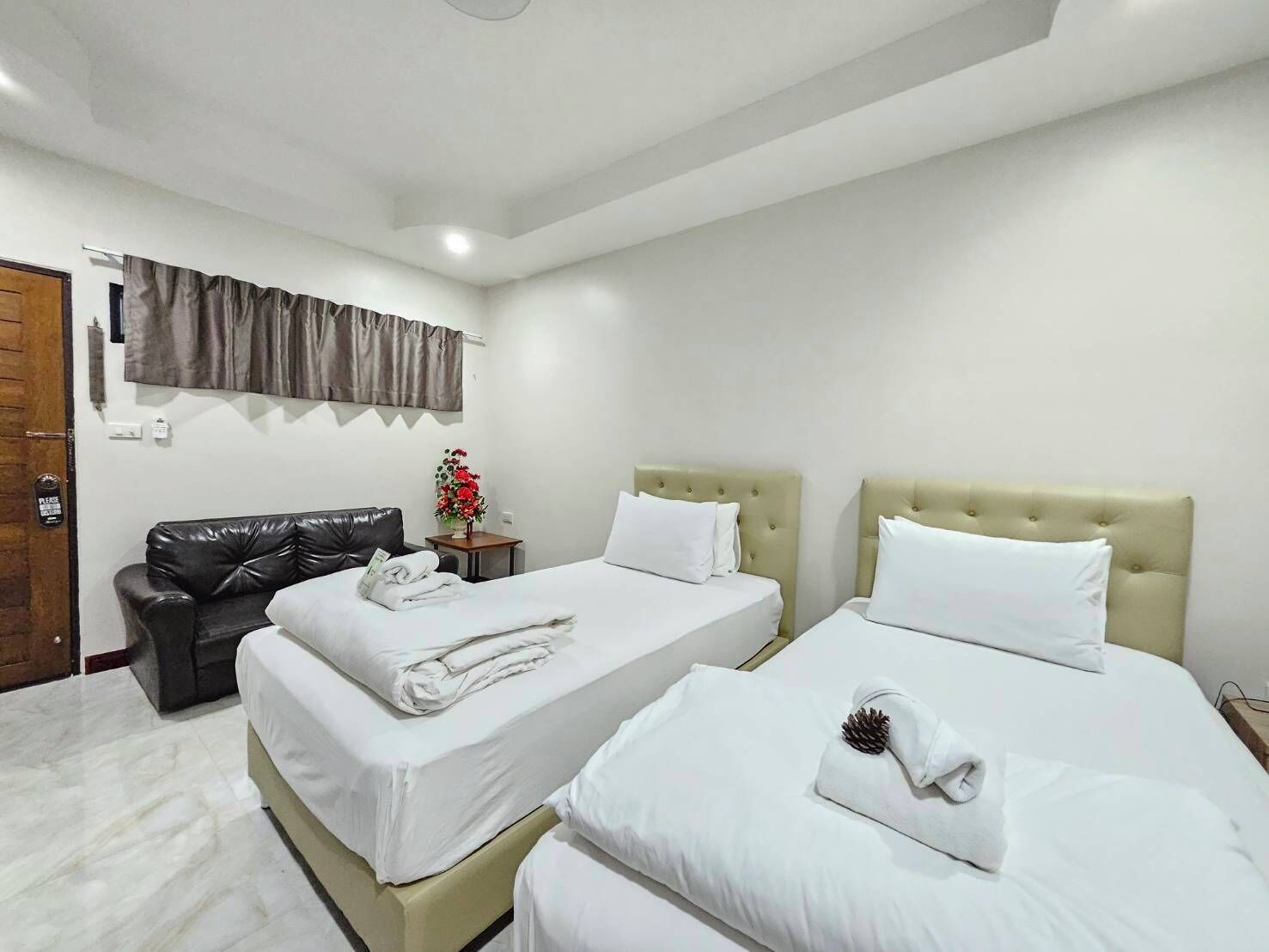 Habitación de hotel con dos camas, un sofá, una mesita con un jarrón de flores y una puerta con un cartel que dice 'Por favor'.