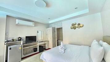 A hotel room with a bed, a desk with a television, a mini-fridge, and an air conditioning unit.