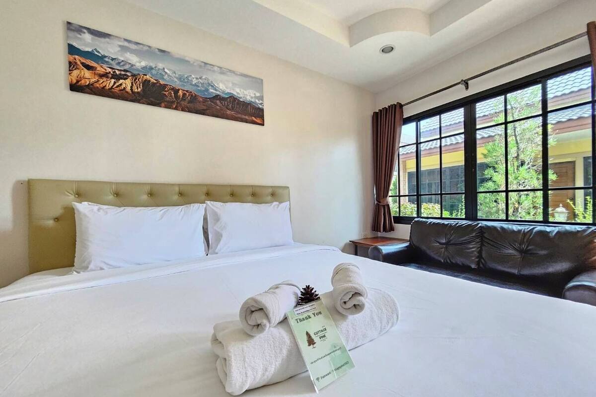 A hotel room with a large bed, a headboard, a window with curtains, and a painting on the wall.