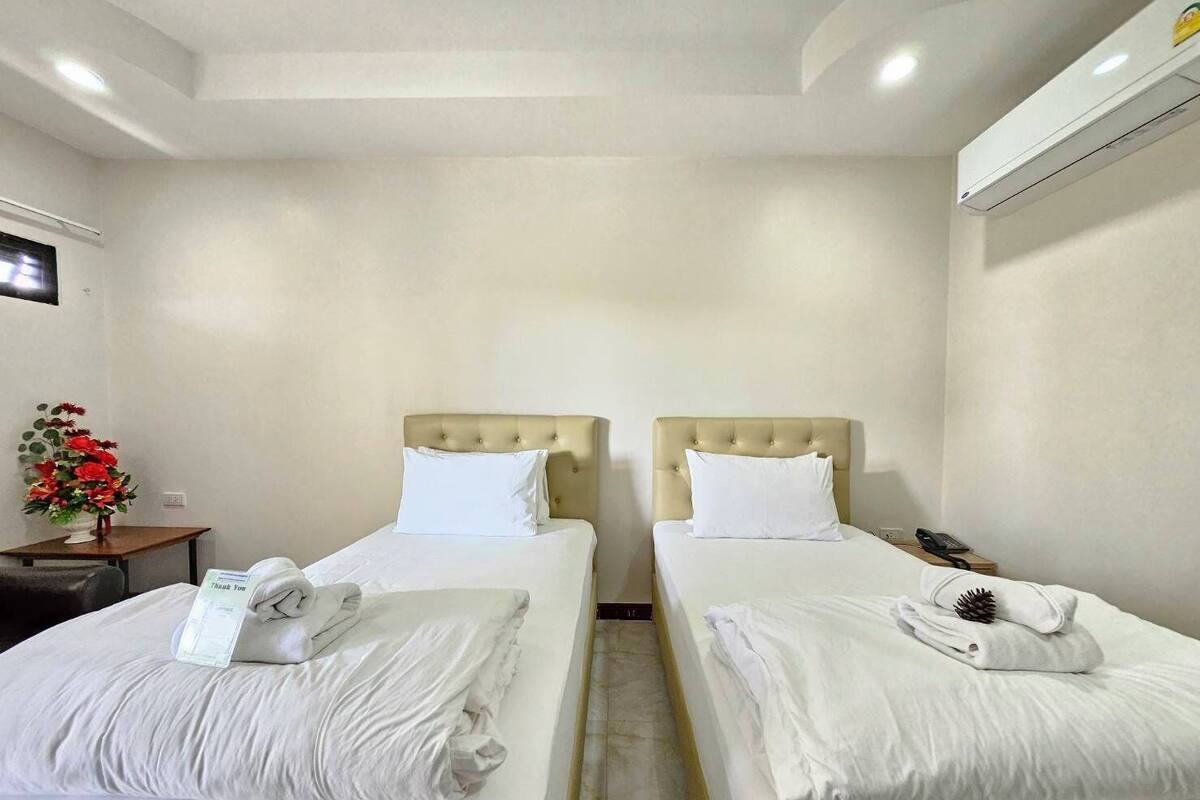 A hotel room with two beds, each with a headboard, white linens, and a small table with a telephone and a vase of flowers.