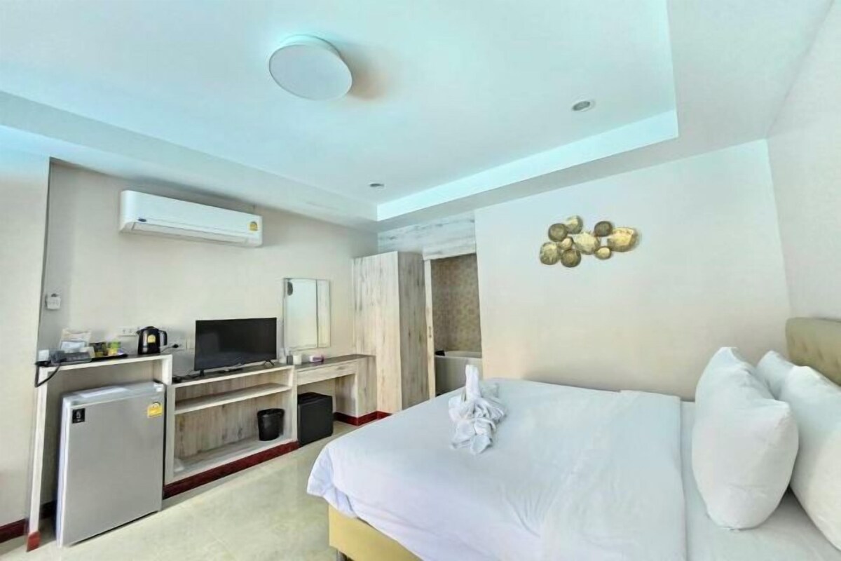 A hotel room with a bed, a desk with a television, a mini-fridge, and an air conditioning unit.