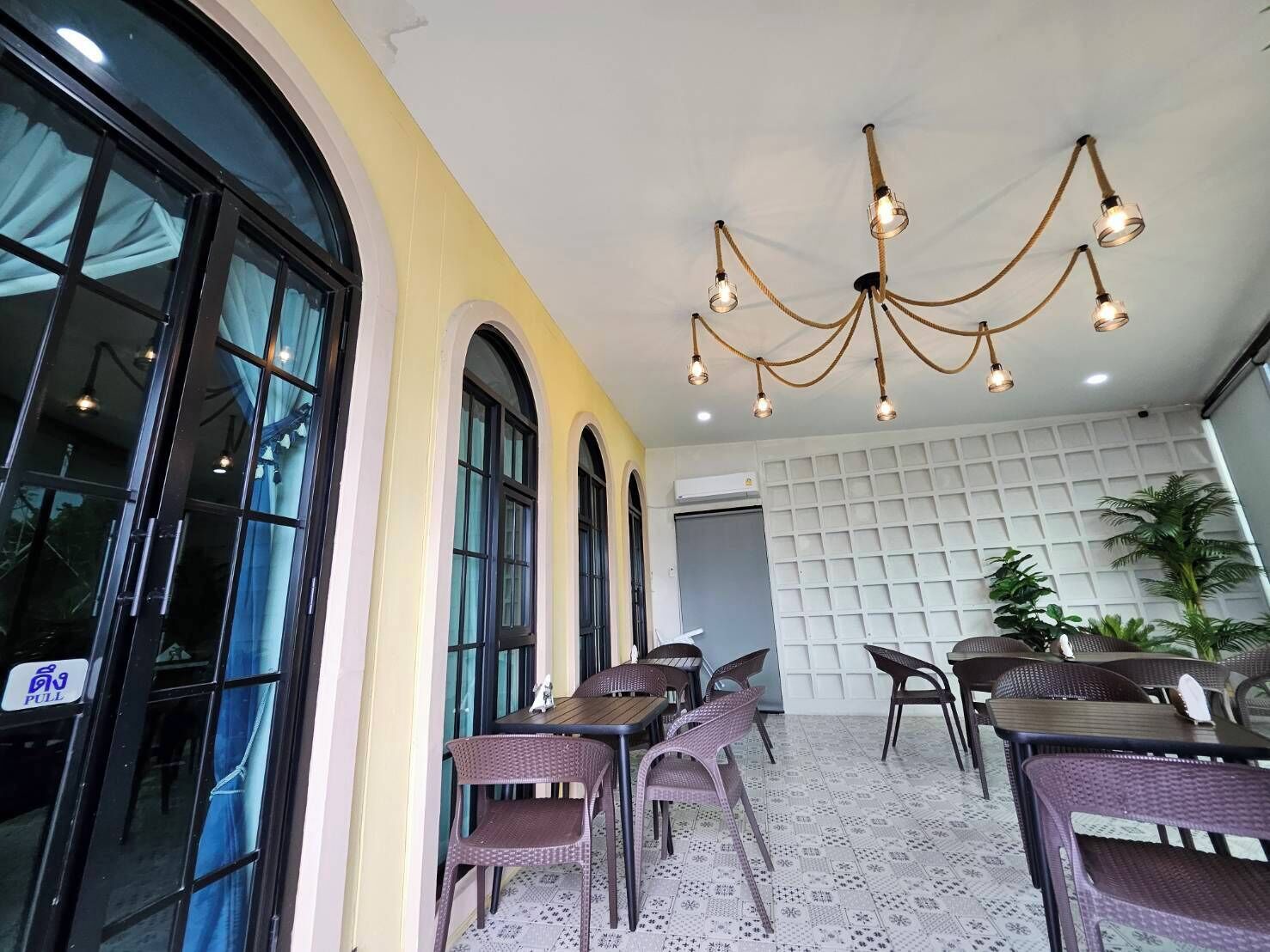 A restaurant with outdoor seating, a chandelier, and a white wall with a grid pattern.
