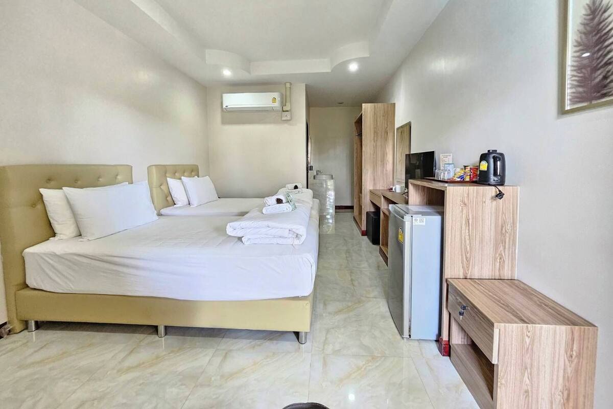A hotel room with two beds, a small kitchenette, a TV, and a refrigerator.