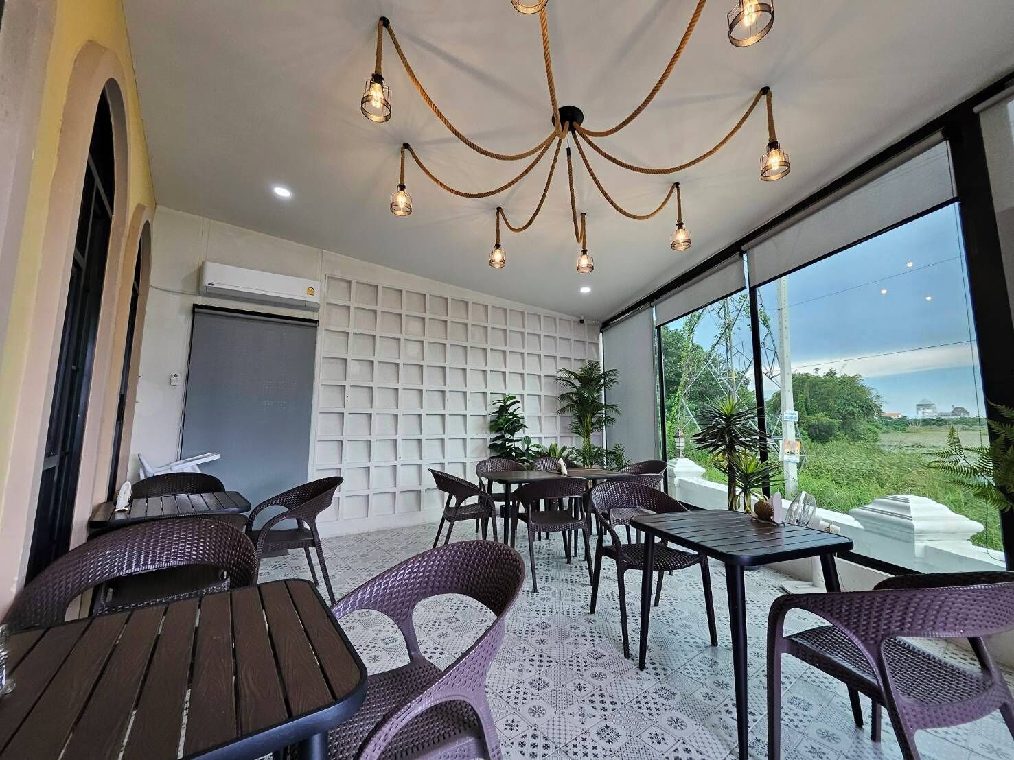 A modern dining area with wicker furniture, a white grid wall, and large windows offering a view of greenery.