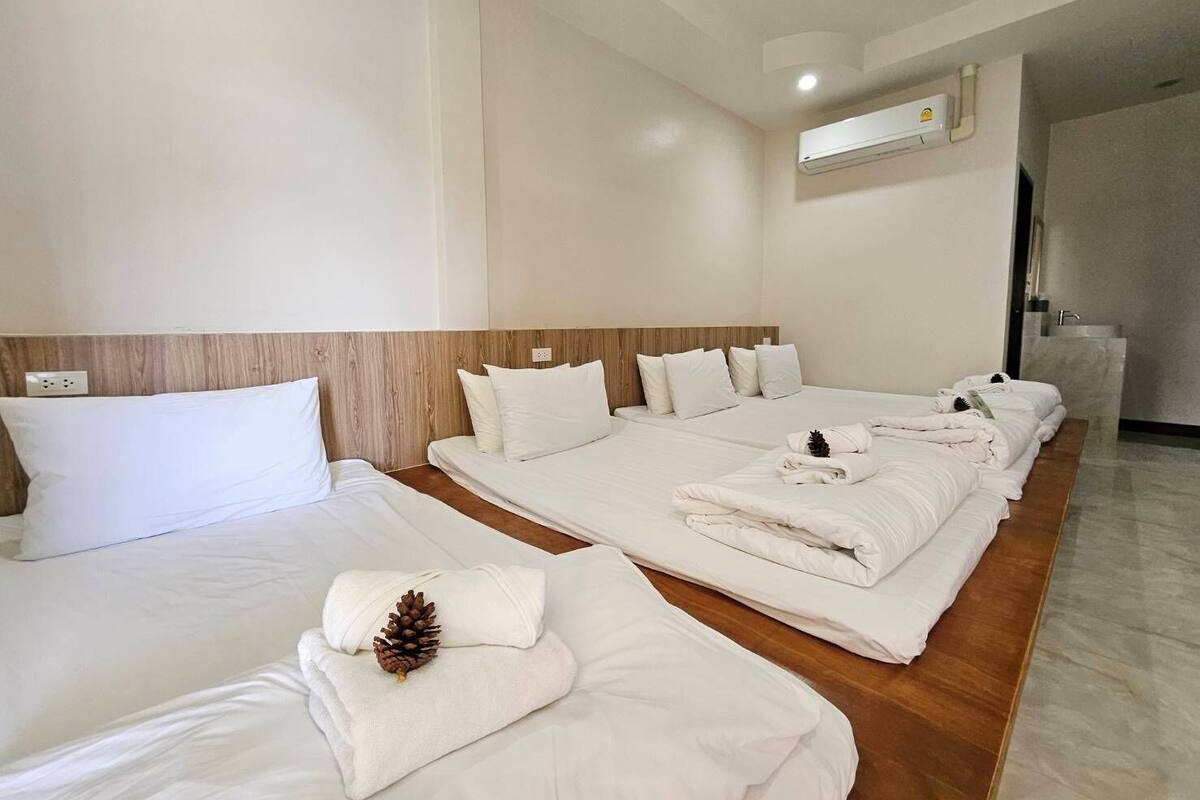 A hotel room with three beds, a wooden headboard, white bedding, and a pine cone decoration.