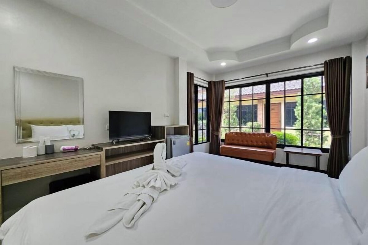 A hotel room with a large bed, a television, a desk with a computer, and a window with curtains.