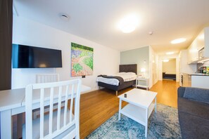 Ein modernes, helles Zimmer mit Bett, Fernseher, Schreibtisch und einer Couch.