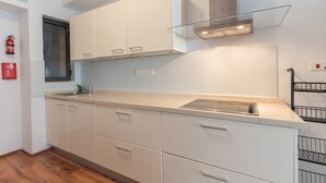 Une cuisine moderne avec des meubles blancs, un évier en acier inoxydable et une étagère en verre au-dessus de la cuisinière.