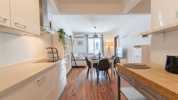 Une cuisine moderne avec des meubles blancs, un plan de travail en bois et un coin repas comprenant une table et des chaises.