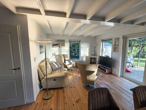 Una sala de estar moderna con un sofá, sillas, un televisor y un ventanal grande.