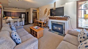 A living room with a fireplace, a dining area, and a kitchen in the background. - 2 bedroom condo, very close to ski-in/out trails and in walking distance to village core (Sun Peaks)
