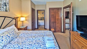 A hotel room with a bed, a TV, a wooden wardrobe, and a bathroom visible through an open door. - 2 bedroom condo, very close to ski-in/out trails and in walking distance to village core (Sun Peaks)