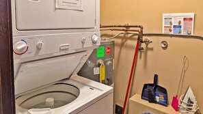 A laundry area with a washing machine, a dryer, and a water heater. There are also cleaning supplies and a red hose. - 2 bedroom condo, very close to ski-in/out trails and in walking distance to village core (Sun Peaks)