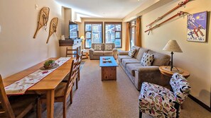 A living room with a sofa, armchair, coffee table, and a dining area with a table and chairs. - 2 bedroom condo, very close to ski-in/out trails and in walking distance to village core (Sun Peaks)