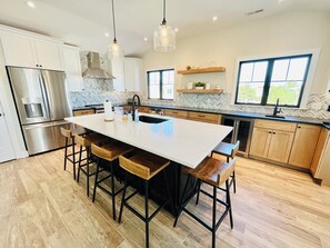 A modern kitchen with a large island, stainless steel appliances, wooden bar stools, and pendant lighting. - RENOVATED HOME ON THE OCEAN BLOCK! (Bethany Beach)