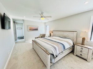 A bedroom with a bed, bedside tables, a ceiling fan, a TV mounted on the wall, and a window with blinds. - RENOVATED HOME ON THE OCEAN BLOCK! (Bethany Beach)
