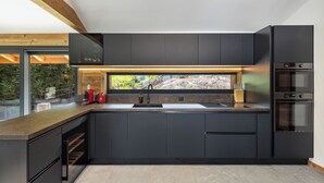 A modern kitchen with dark cabinetry, a large window, and built-in appliances. - Chalet Le Reve Cinema Room Jacuzzi (Riddes)