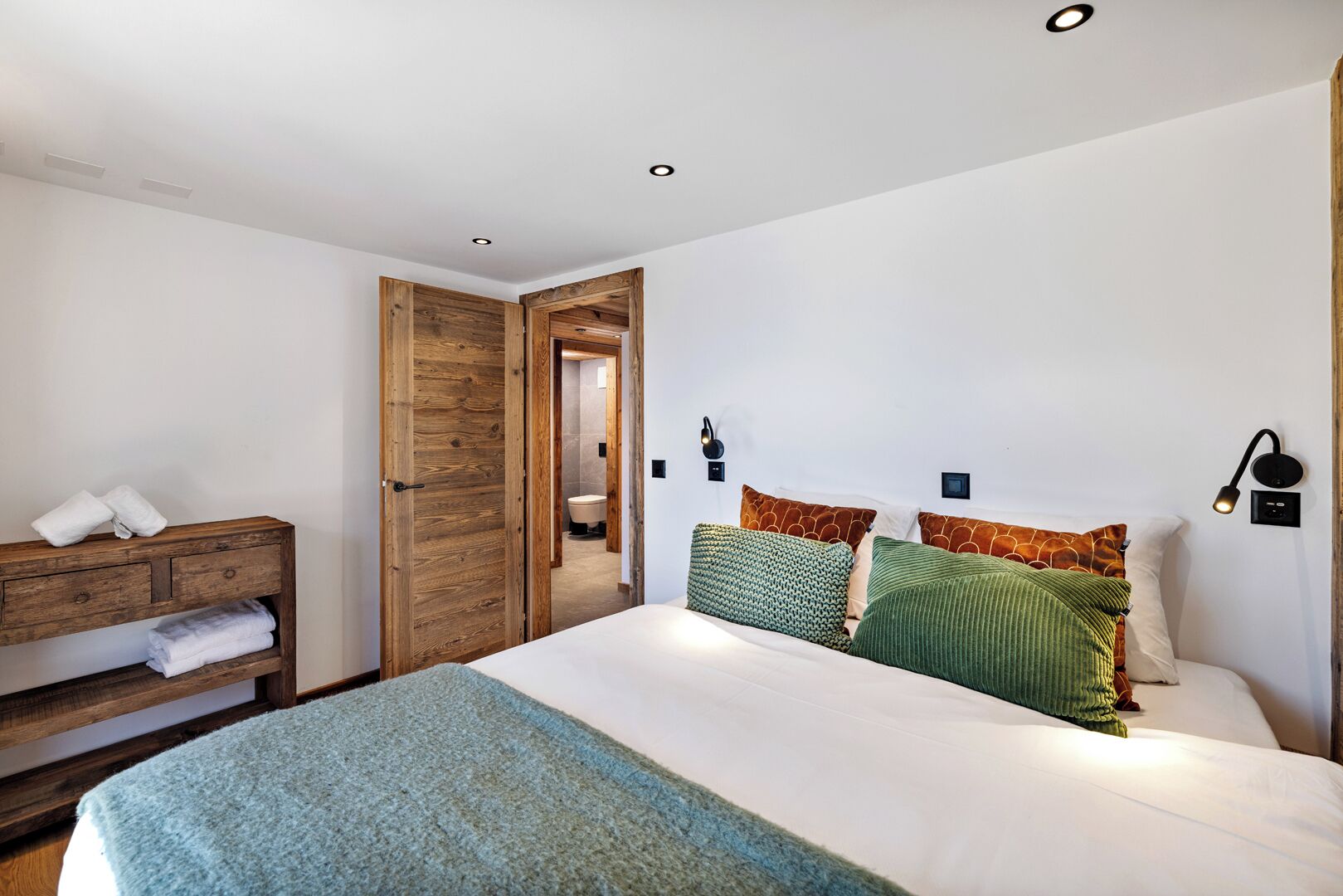 Un dormitorio con un armario de madera, una cama con almohadas verdes y marrones, y una alfombra azul.