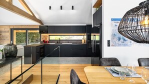 A modern kitchen with dark cabinetry, a stainless steel refrigerator, and a dining area with a wooden table and chairs. - Chalet Le Reve Cinema Room Jacuzzi (Riddes)