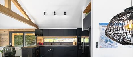 A modern kitchen with dark cabinetry, a stainless steel refrigerator, and a dining area with a wooden table and chairs.