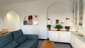 Ein Wohnzimmer mit grauem Sofa, einem Holztisch und einer weißen Kommode mit Blumentöpfen.