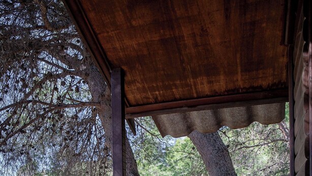 Una terraza de madera con una mesa y una silla de metal, con vistas a un paisaje montañoso.