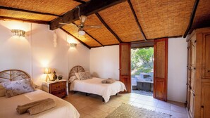 Una habitación con dos camas, ventilador de techo, mesita de noche con lámpara y armario de madera.