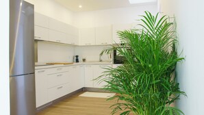 Une cuisine moderne avec des meubles blancs, un réfrigérateur en acier inoxydable et une grande plante verte.