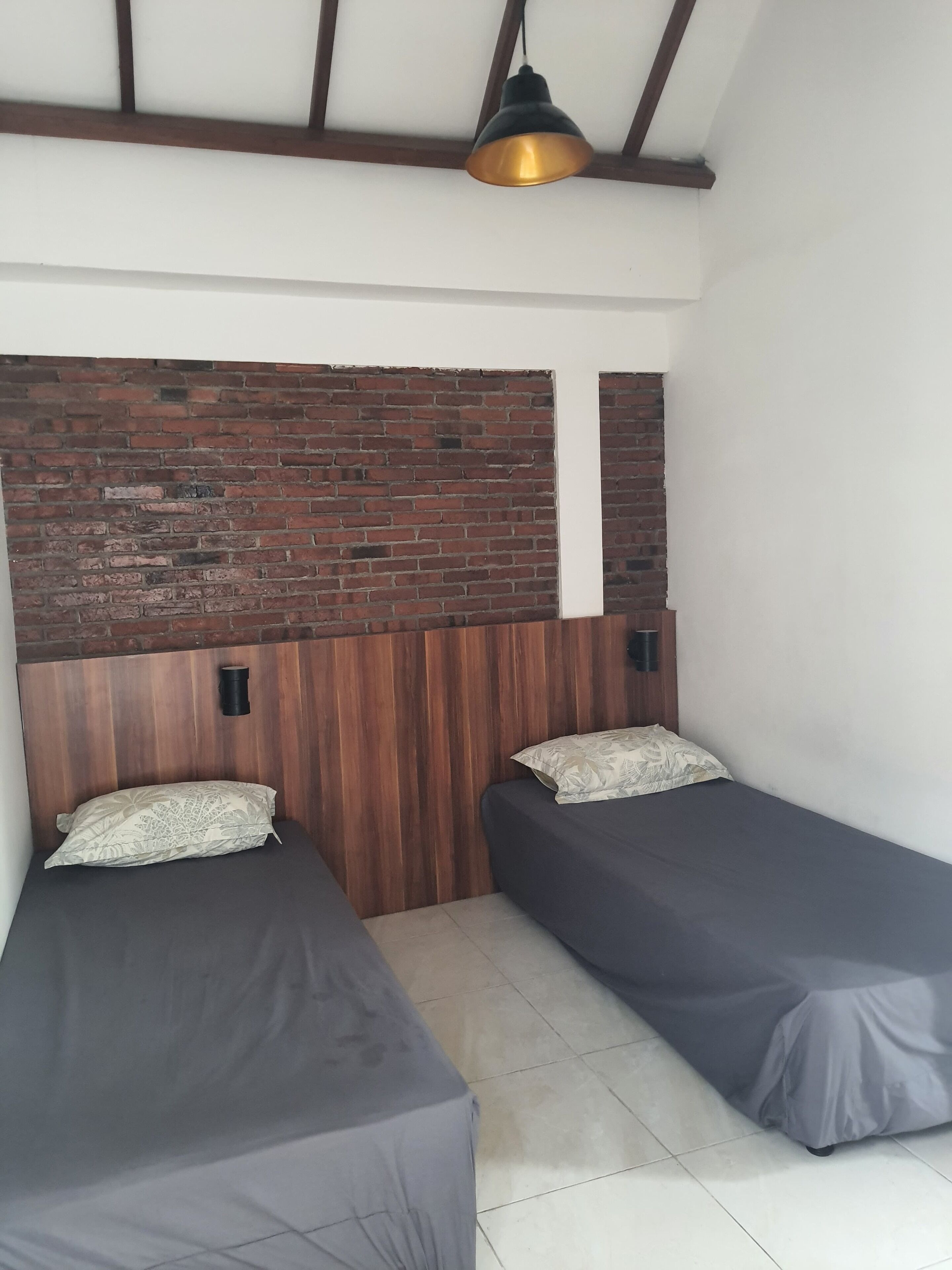 Ein Zimmer mit zwei Einzelbetten, einer Ziegelwand, einem hölzernen Kopfteil und einer hängenden Pendelleuchte.