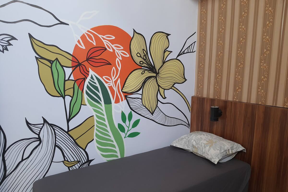 A room with a bed, a wall mural with floral and leaf patterns, and a wooden headboard.