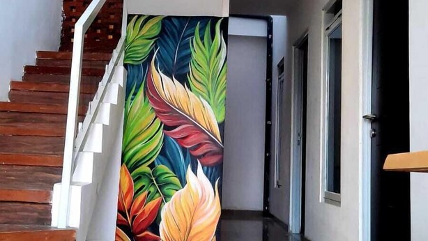 A hallway with a staircase, a colorful leaf mural, and a polished floor. - Malang And Bromo Tour Backpacker (Malang)