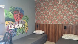 A room with two single beds, a wall with a tropical leaf mural, and a patterned wallpaper. - Malang And Bromo Tour Backpacker (Malang)