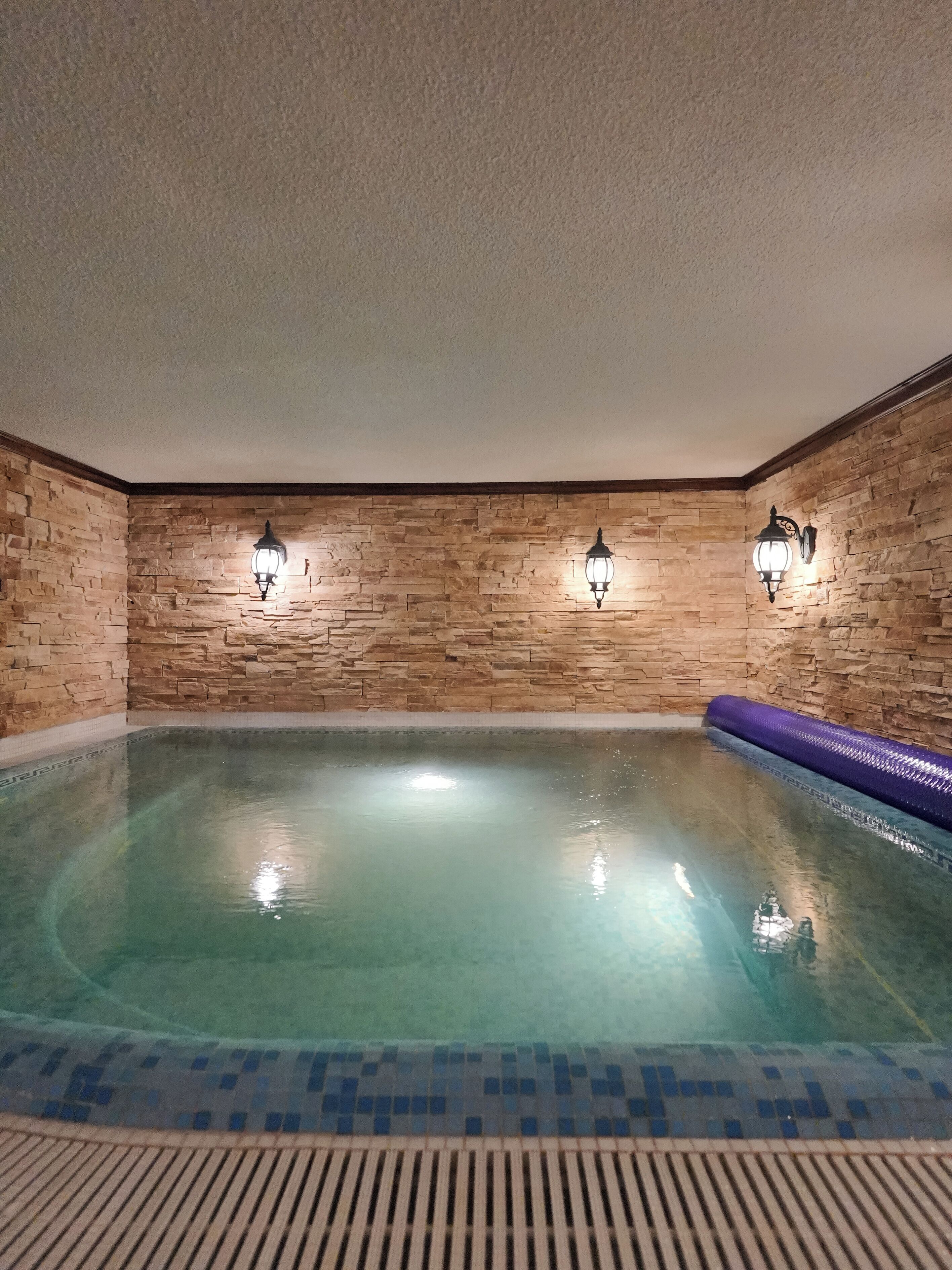 An indoor swimming pool with stone walls and two wall-mounted lights.