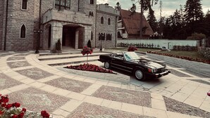 A historic stone building with a courtyard, a classic convertible car, and red flowers. - The Castle - Your unique way of retreat (Samokov)