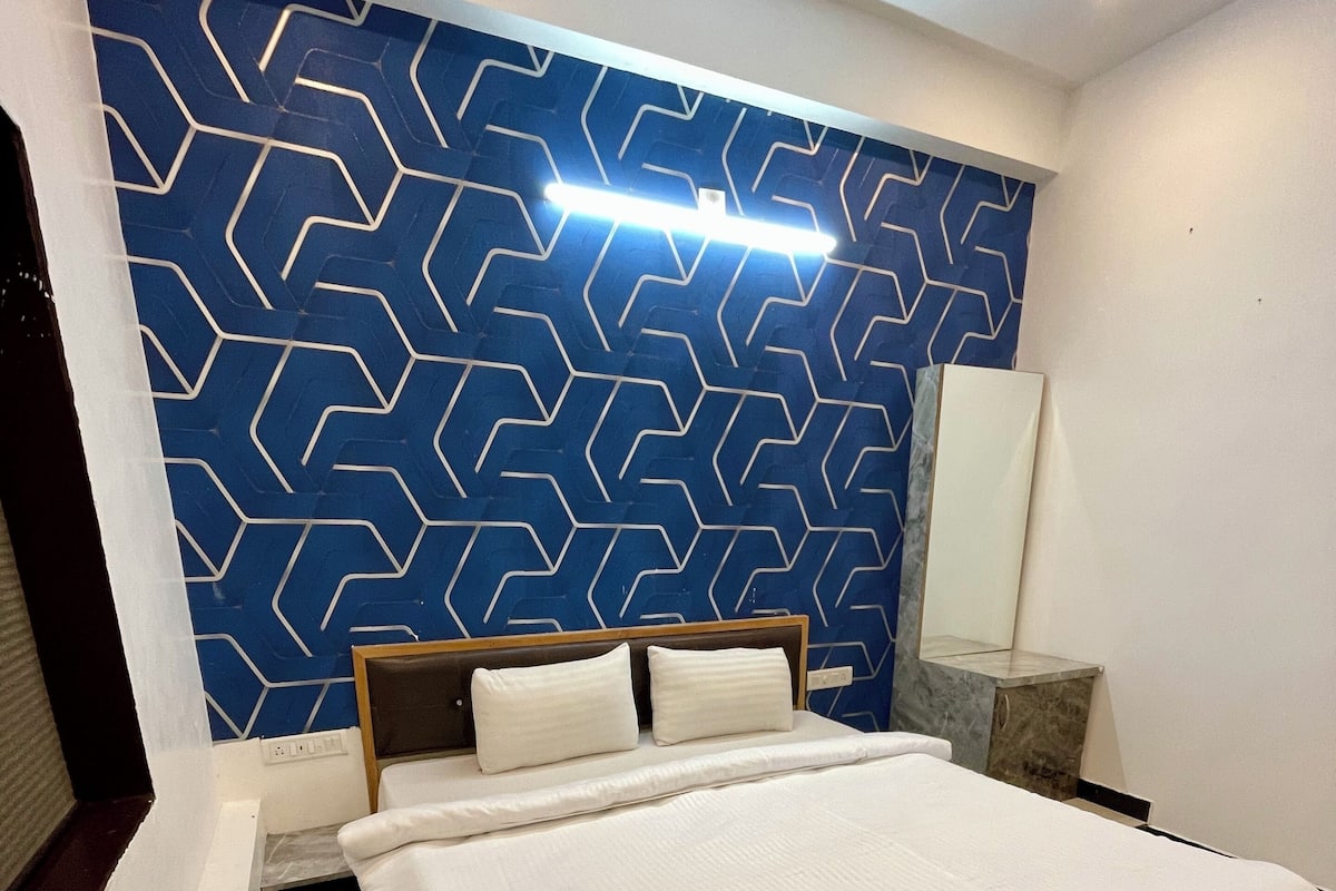 A modern hotel room with a large bed, a blue patterned wall, and a marble bedside table.