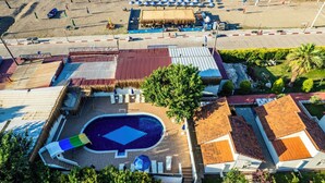 Vue aérienne d’un complexe hôtelier avec une piscine, des parasols de plage et un bâtiment à toit de chaume.
