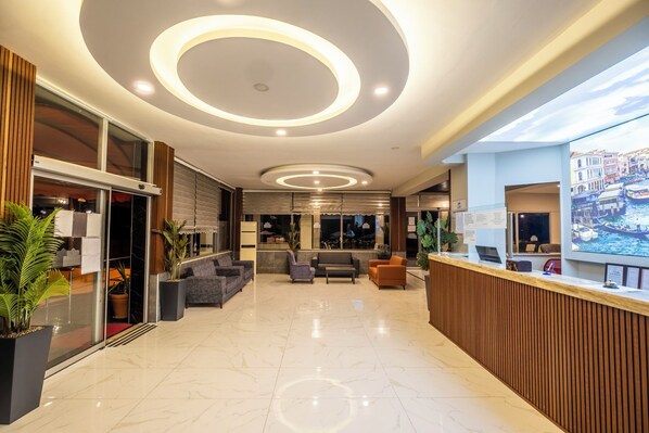 A modern hotel lobby with a reception desk, seating area, and a large window with a cityscape view. - Club Sideris Halal Family Hotel & Spa (Menderes)
