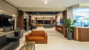 Un hall d’hôtel moderne comprenant un comptoir d’accueil, un espace salon et une grande fenêtre donnant sur le paysage urbain.