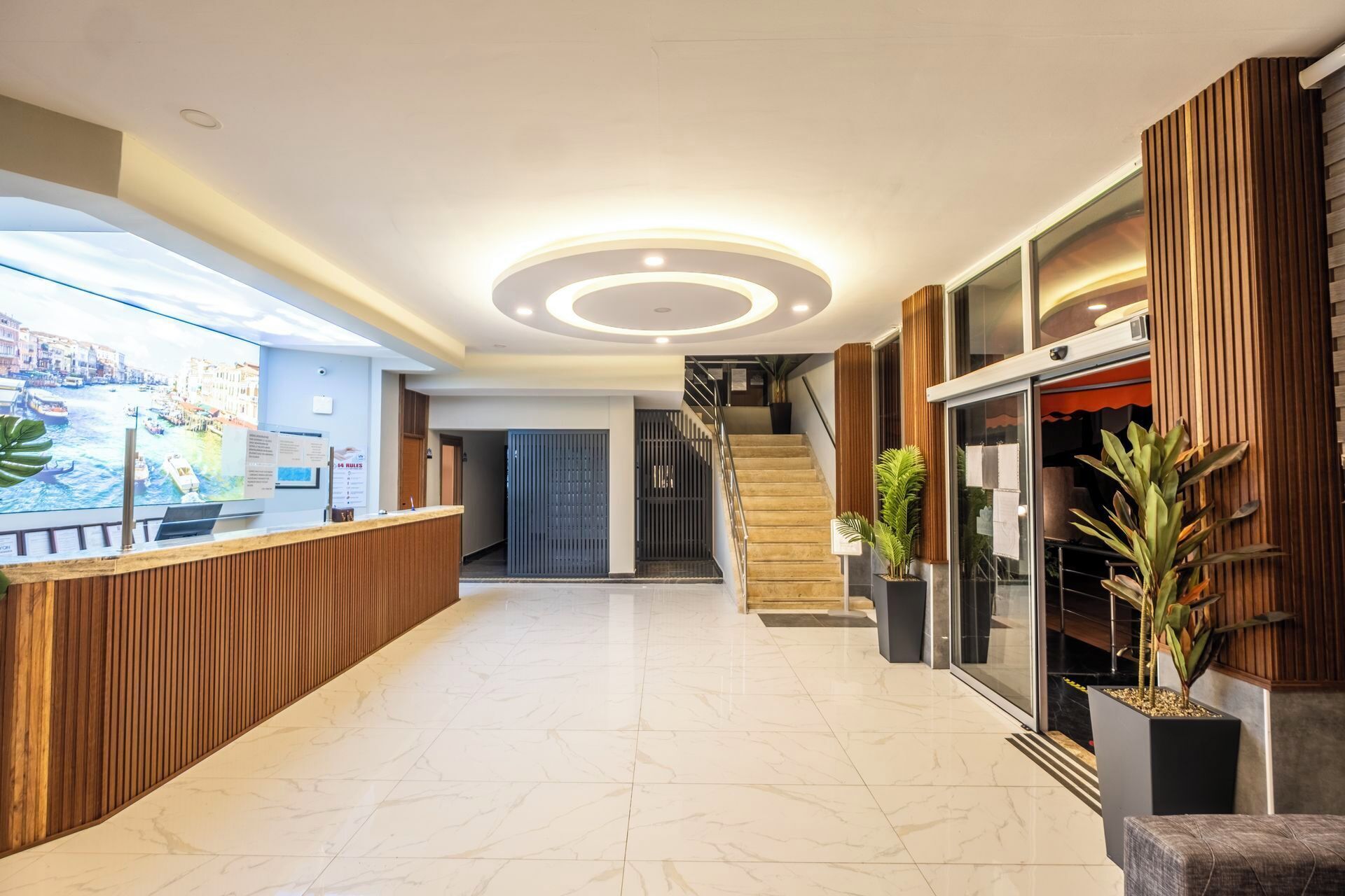 A hotel lobby with a reception desk, a staircase, and potted plants.