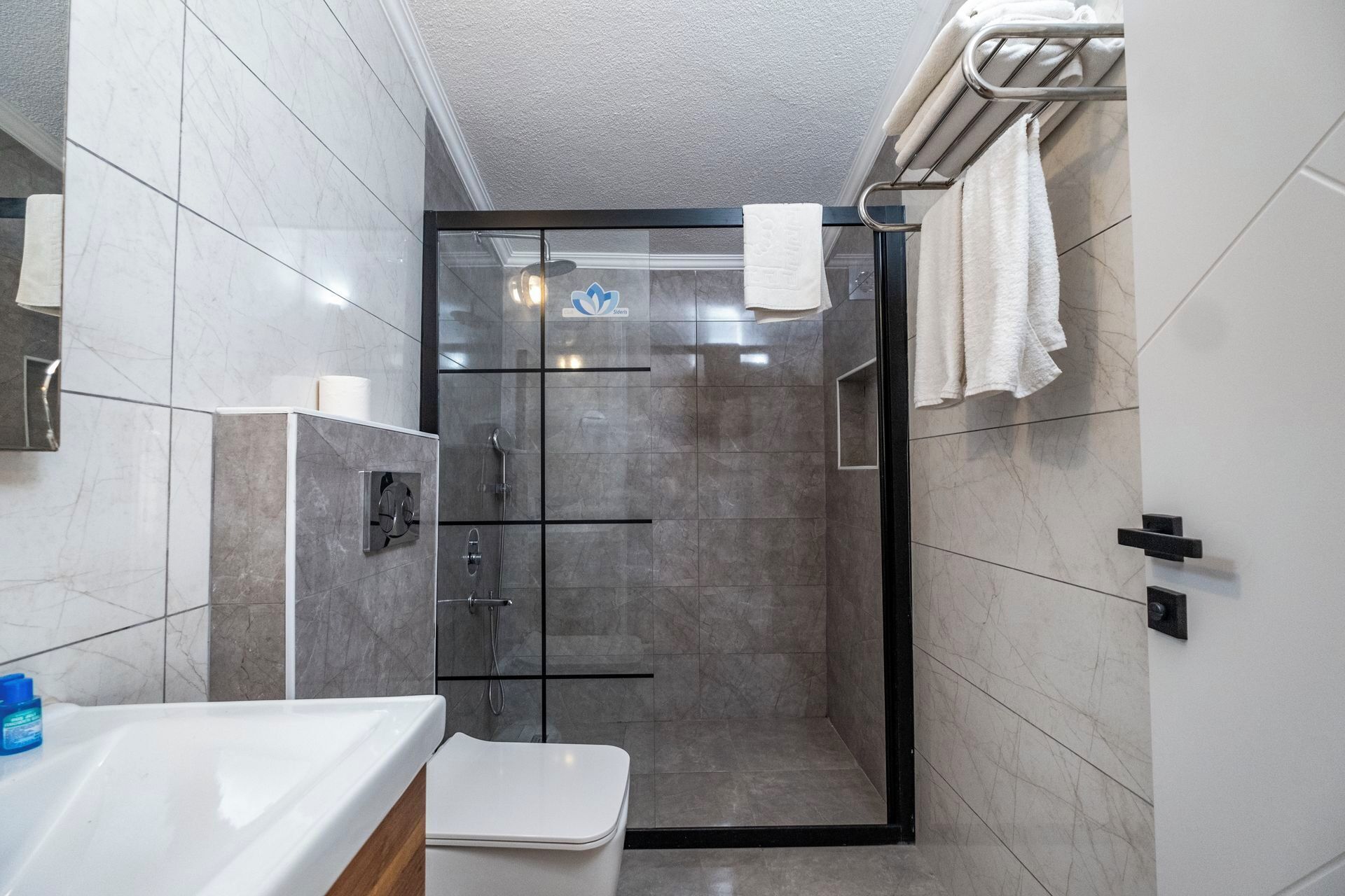 Een moderne badkamer met een douchecabine van glas, witte tegels en een zichtbaar toilet.