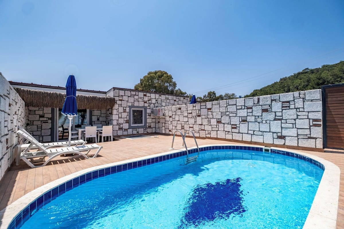 Una piscina con muretto in pietra e lettini da relax.