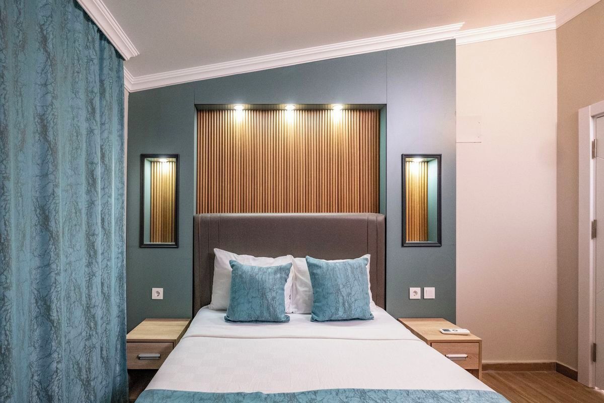 A hotel room with a large bed, two bedside tables, a wooden headboard, and wall-mounted lighting.