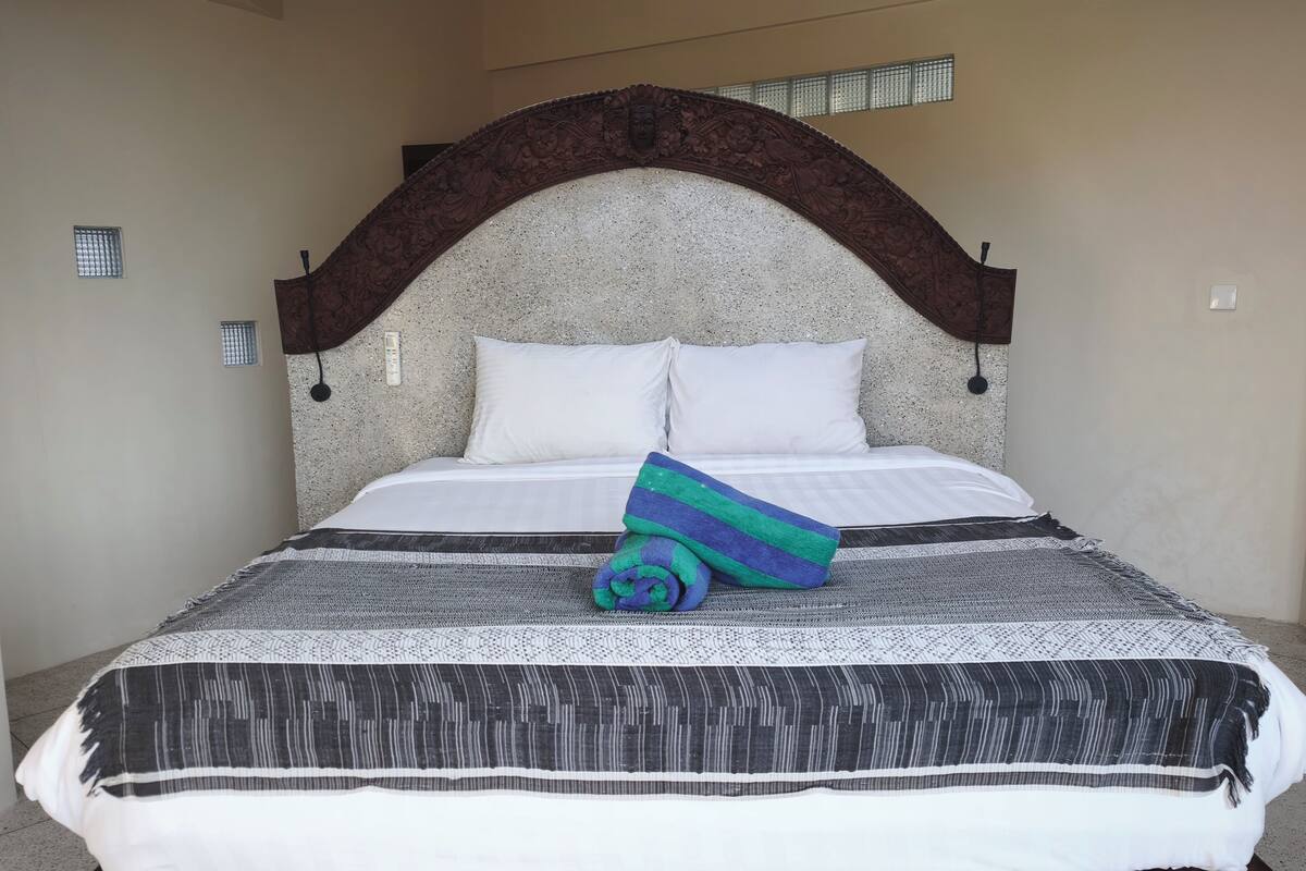 Een bed met hoofdbord, twee kussens, een deken en een opgerolde handdoek.