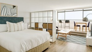 Ein modernes Hotelzimmer mit einem großen Bett, einem Schreibtisch mit Stühlen, einem Bücherregal und einem großen Fenster.